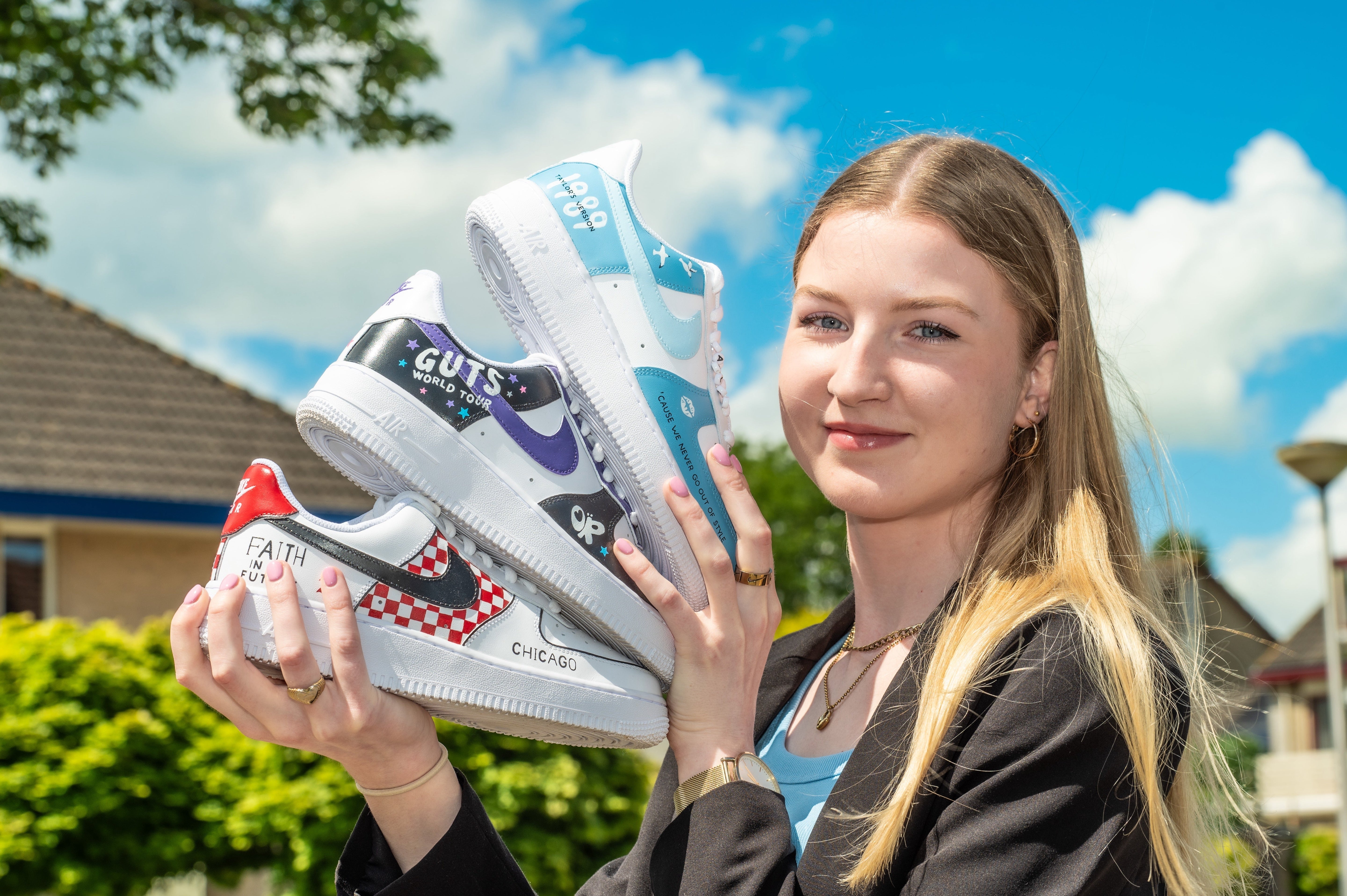 Photo of artist, Custom by Sara, holding three pairs of Nike AF1 sneakers she hand-painted custom designs onto
