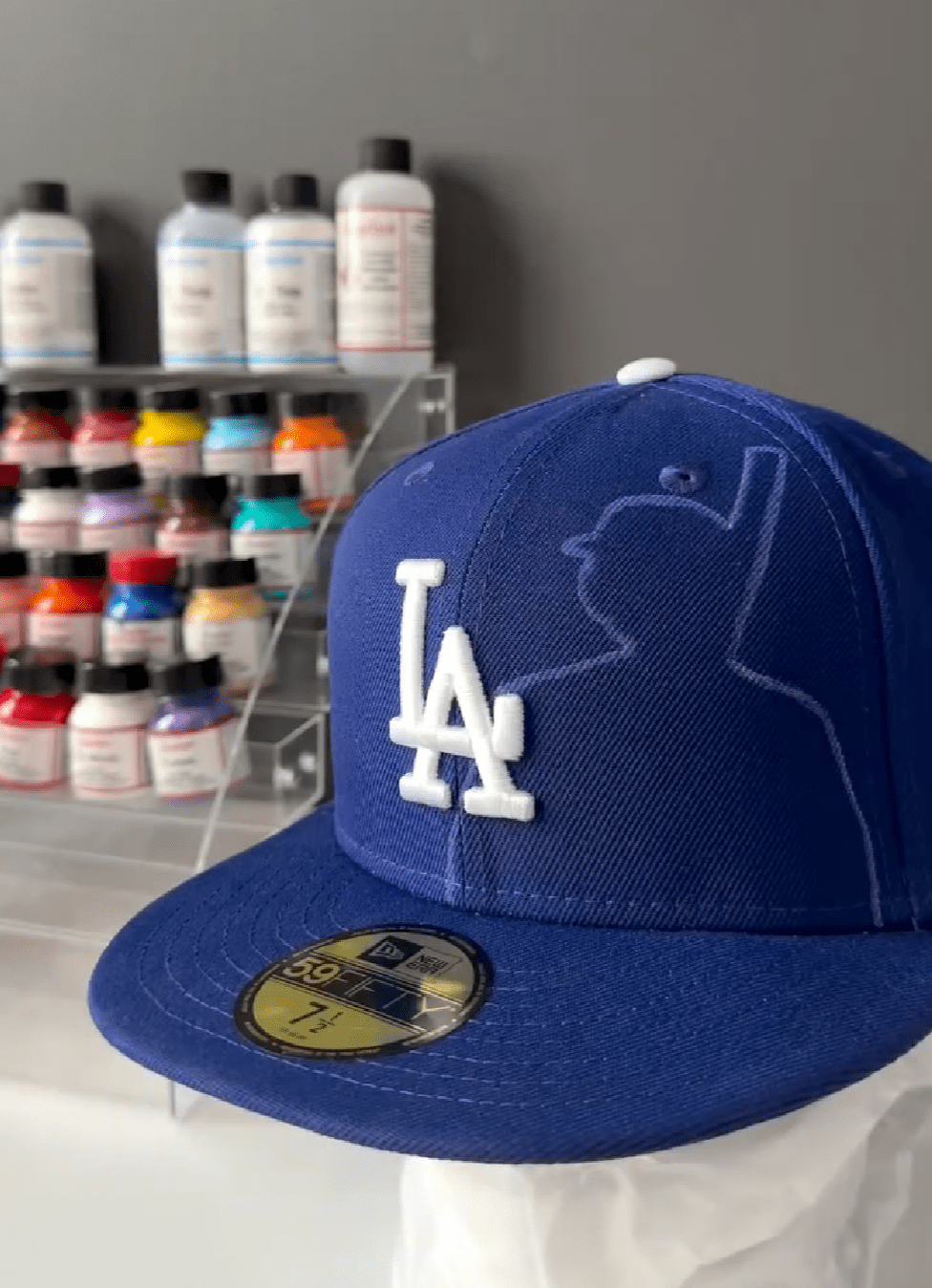 Image shows a close-up of someone using a cotton pad and bottle of Angelus Easy Cleaner and/or Leather Preparer & Deglazer to clean a fabric or leather hat panel before painting.