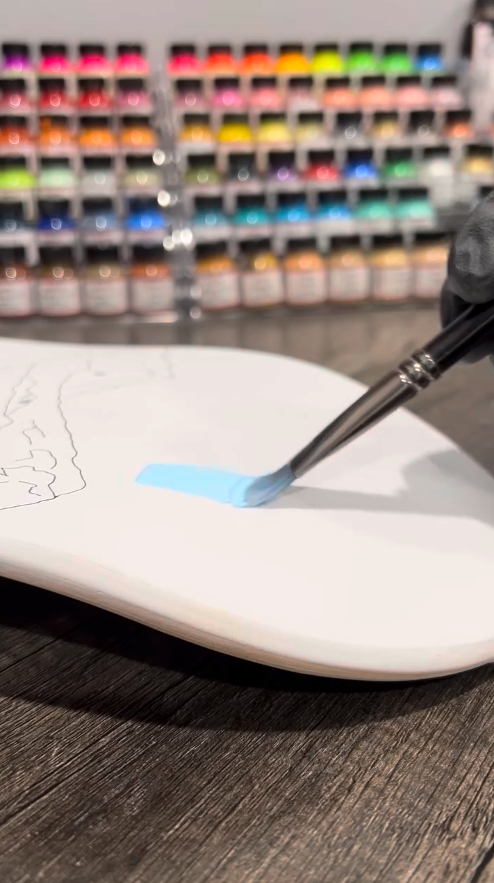 Painting with Pale Blue Angelus Paint on a skateboard with sketched design.