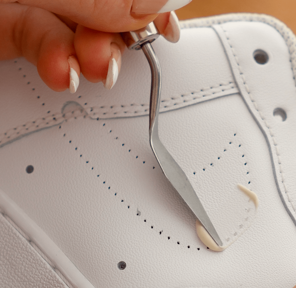 Spatula applying a thin layer of Angelus paintable repair filler directly into a hole in white leather, ensuring even coverage