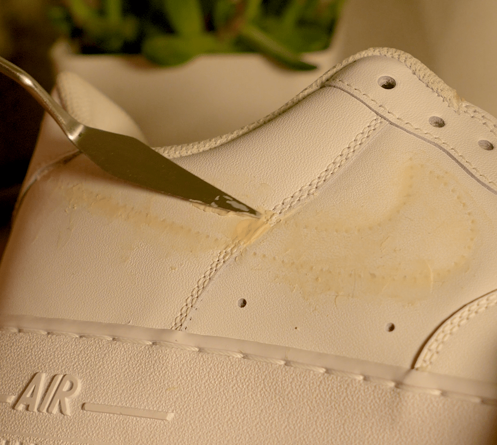 Light‑grit sandpaper smoothing the dried filler over a leather surface, blending the repair into the surrounding area