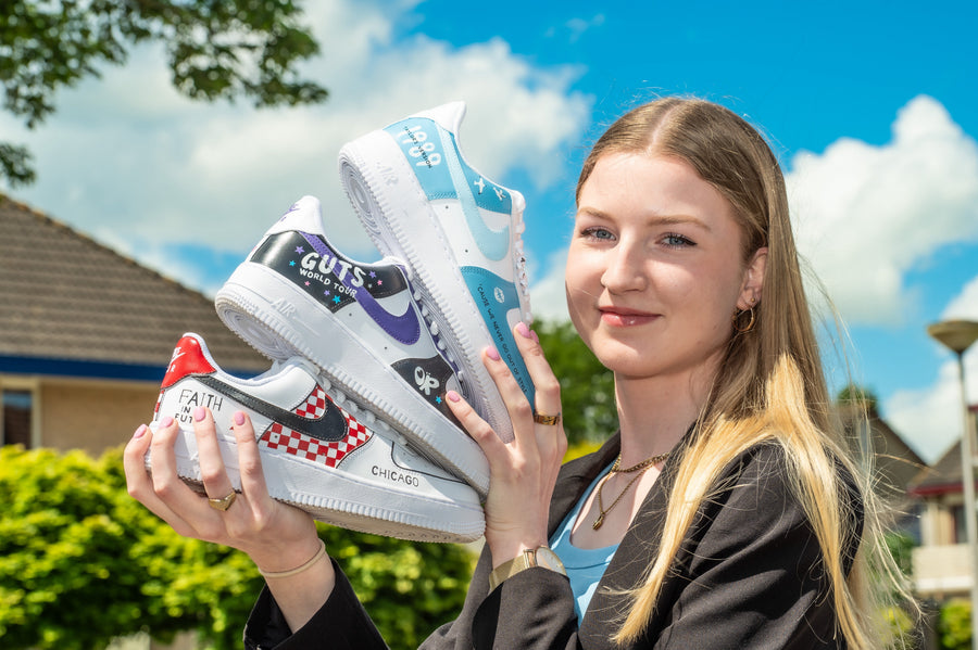 Photo of artist, Custom by Sara, holding three pairs of Nike AF1 sneakers she hand-painted custom designs onto