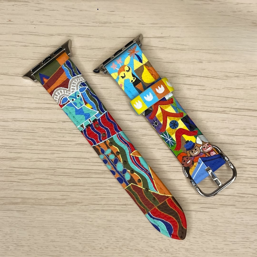A colorful, hand-painted leather watch band featuring intricate, folk-art-style illustrations. The design includes vibrant depictions of animals, figures, and abstract patterns in primary colors.