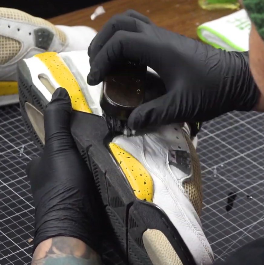 Brushing shoe cement along the midsole of a separated white and yellow sneaker sole