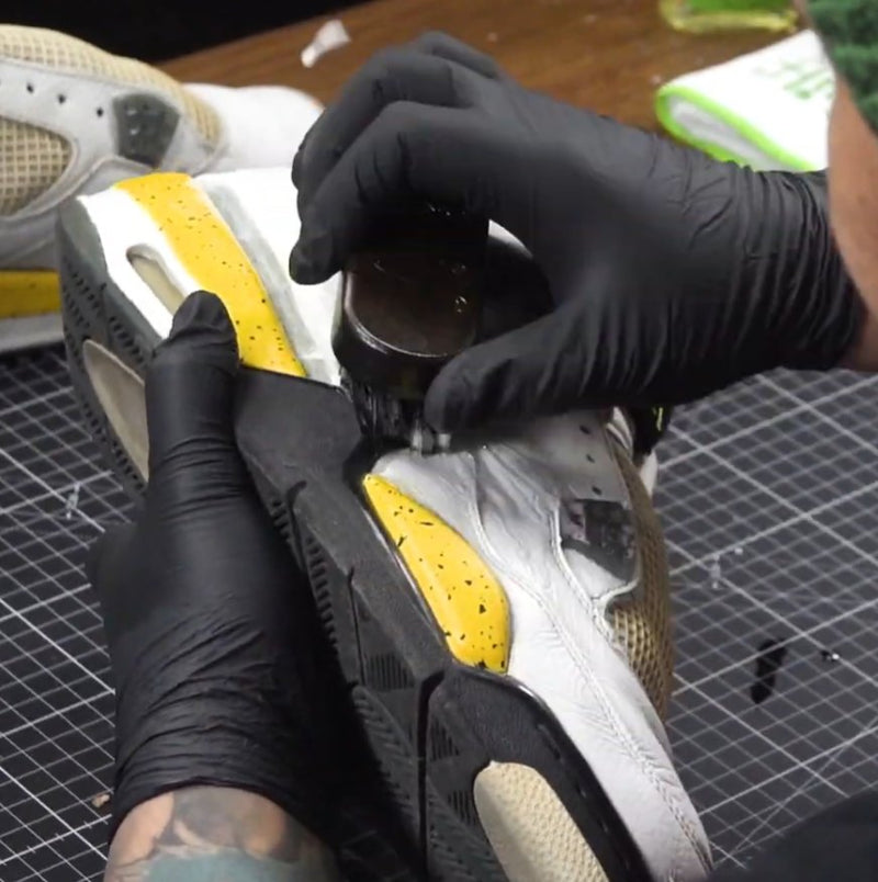 Brushing shoe cement along the midsole of a separated white and yellow sneaker sole