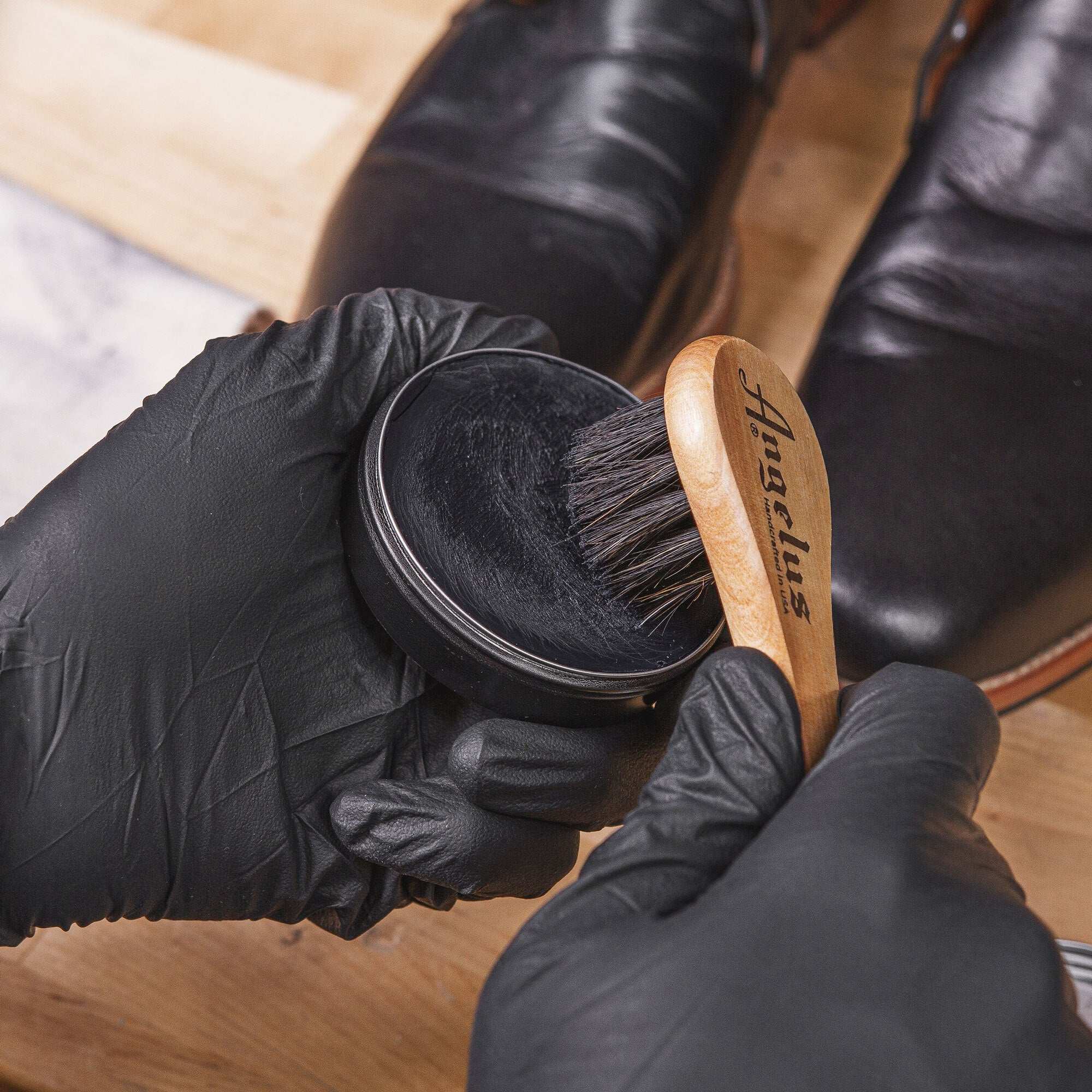 Wax applicator brush applying shoe wax polish to leather boots.