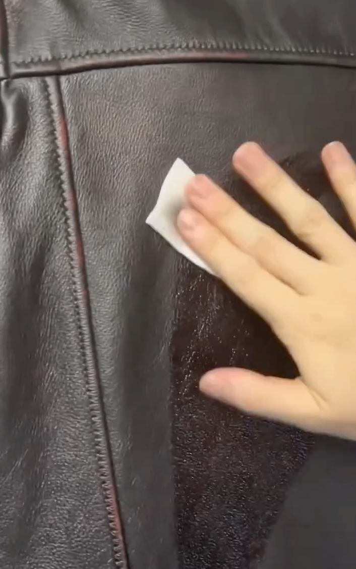 Wiping a brown leather jacket with Angelus Leather Preparer and Deglazer to prep for paint