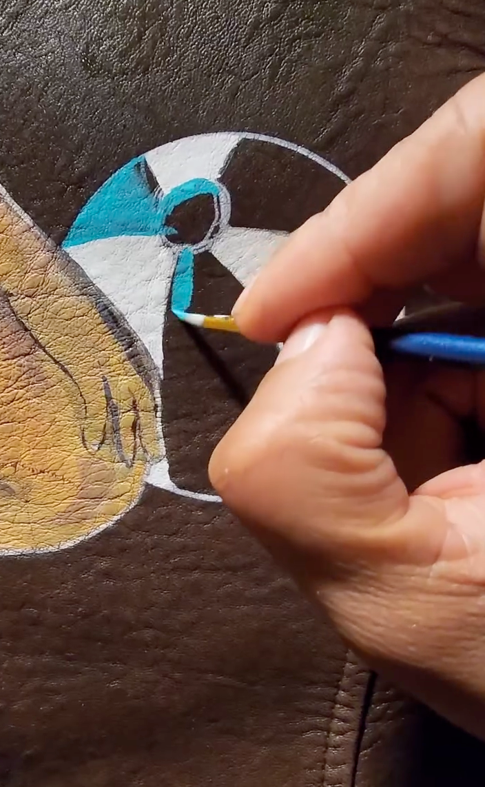 Artist applying Angelus leather paint to a custom bomber jacket with a fine detail brush